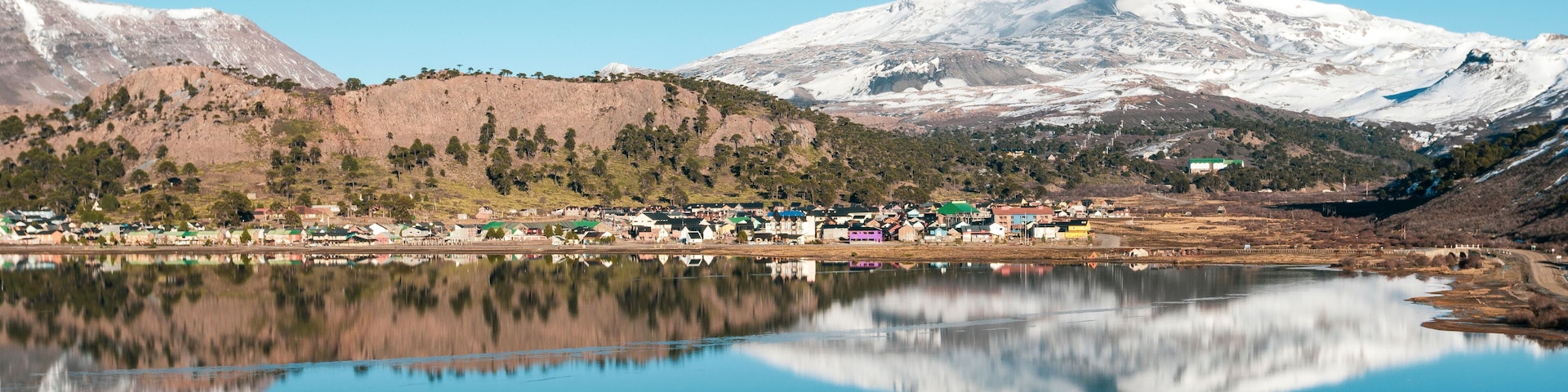 A lake reflecting a town and snow-capped mountains.