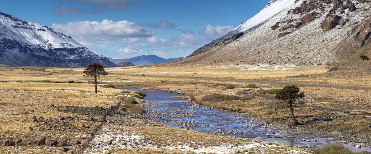 A mountainous landscape with a river, sparse vegetation, and a clear sky.