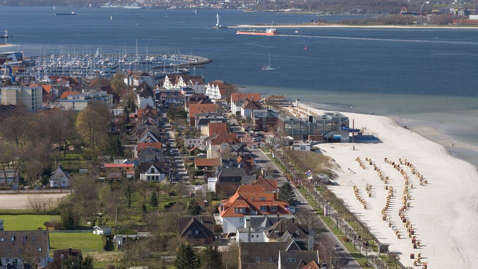 A coastal town with a sandy beach, residential buildings, and a marina with boats.