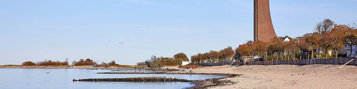 Eine Küstenlandschaft mit einem hohen Backsteinturm, Sandstrand und Herbstbäumen.