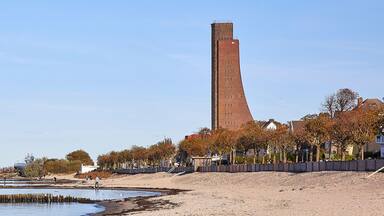 Uma área costeira com uma torre de tijolos alta, praia arenosa e árvores de outono.