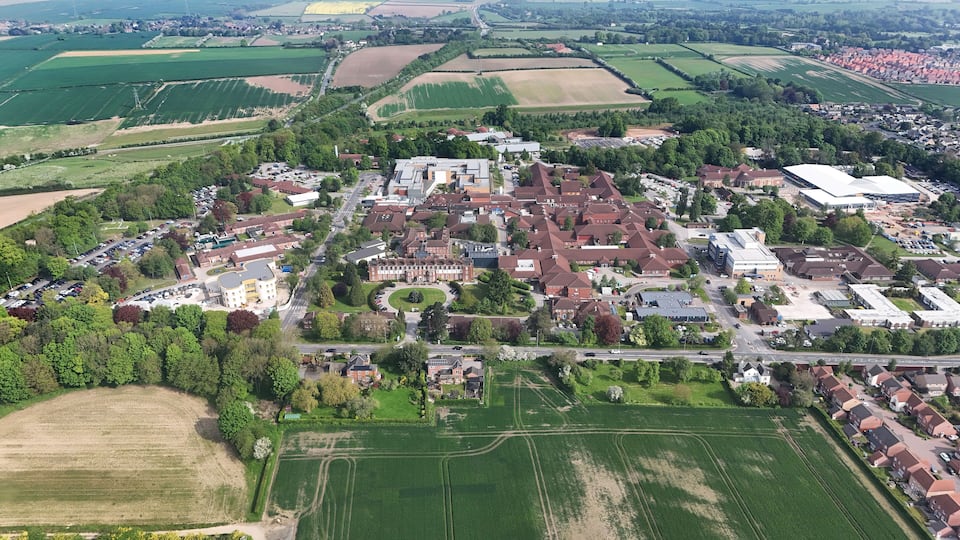 An aerial view of a town with residential areas, green fields, and a large industrial building.