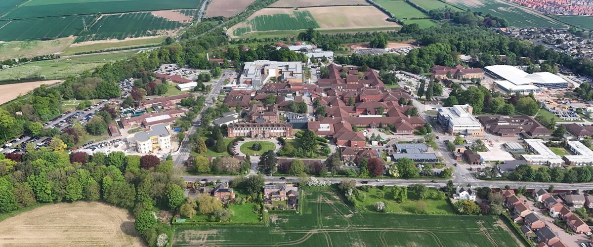 An aerial view of a town with residential areas, green fields, and a large industrial building.