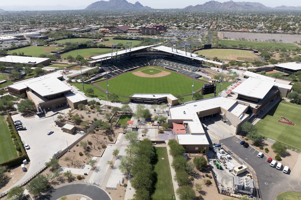A baseball stadium surrounded by mountains and a parking lot.
