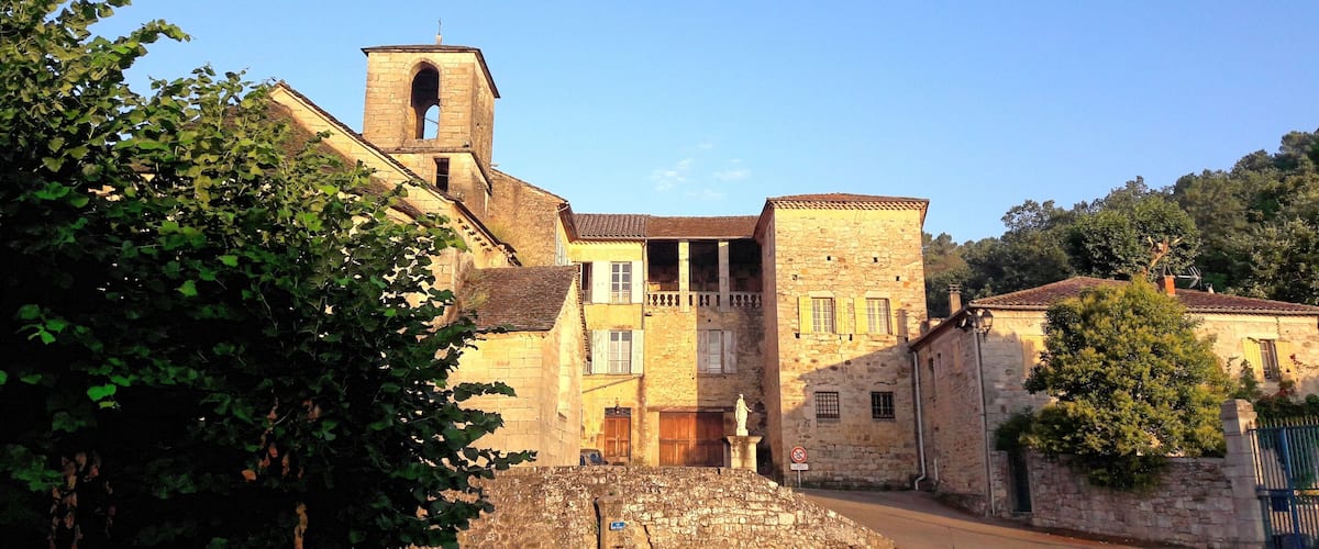 A historic stone building with a bell tower, surrounded by trees and a stone wall.