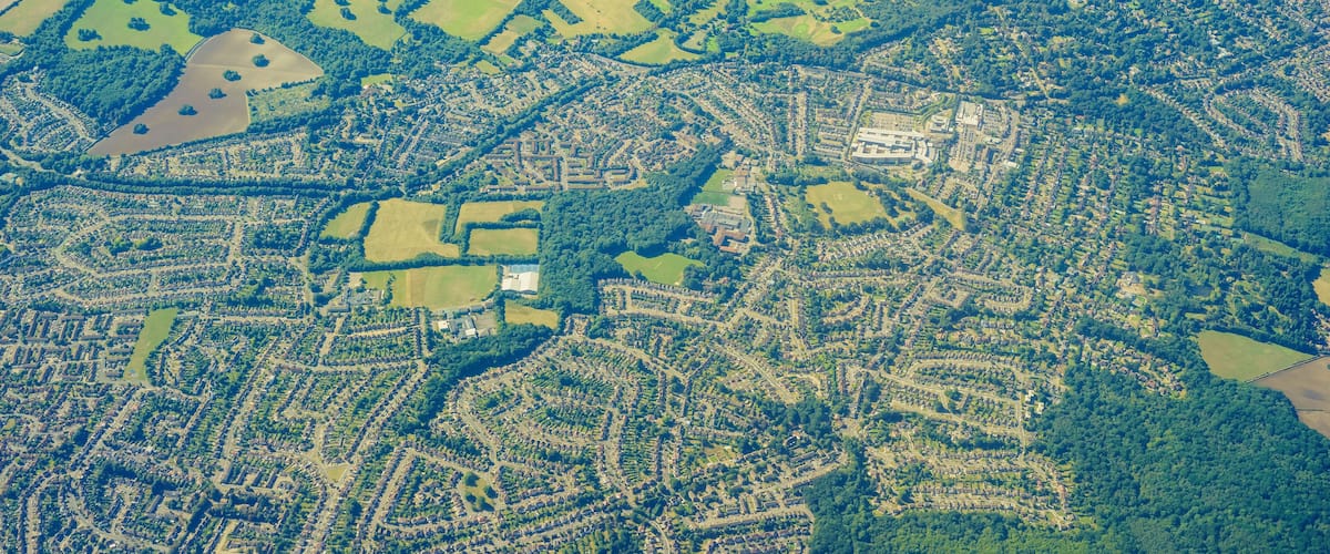 An aerial view of a town with a mix of residential areas, green fields, and patches of forest.