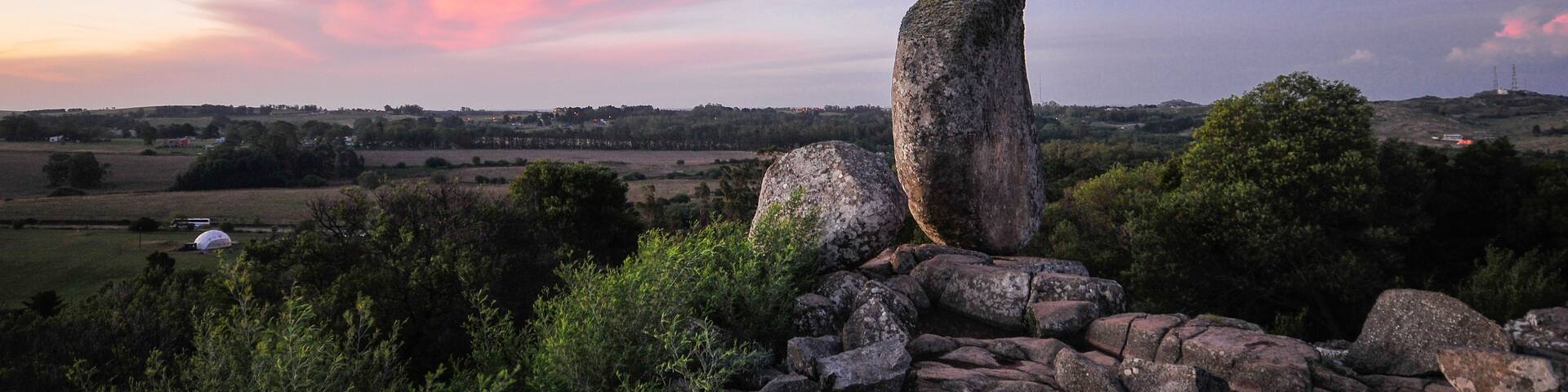 A stone standing on a rocky outcrop with a sunset sky in the background.