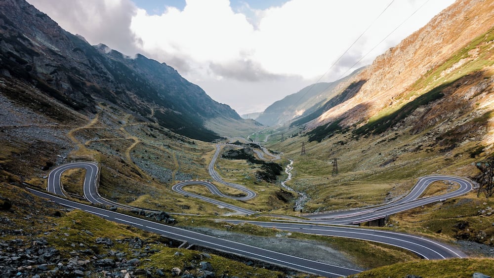 Une route de montagne sinueuse, parsemée de nombreux virages, bordée d’un paysage rocheux et d’une végétation clairsemée.