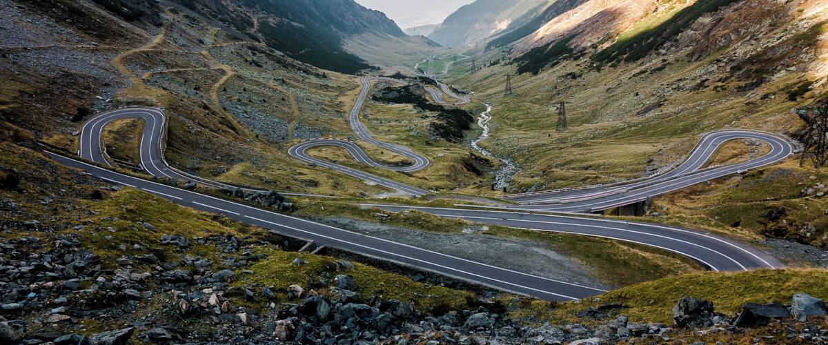 A winding mountain road with multiple curves, surrounded by rocky terrain and sparse vegetation.