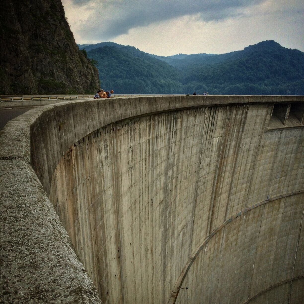 A concrete dam with a curved structure, overlooking a mountainous landscape.