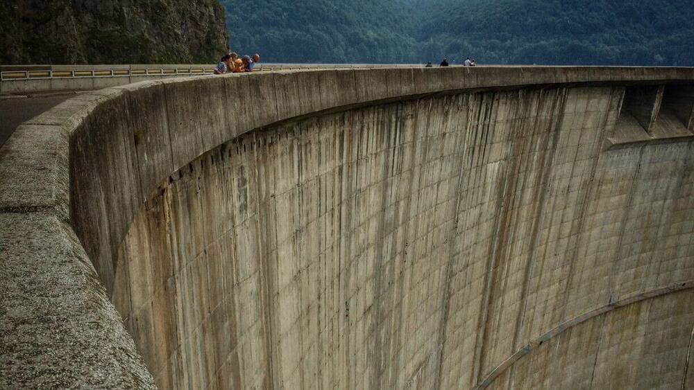 A concrete dam with a curved structure, overlooking a mountainous landscape.