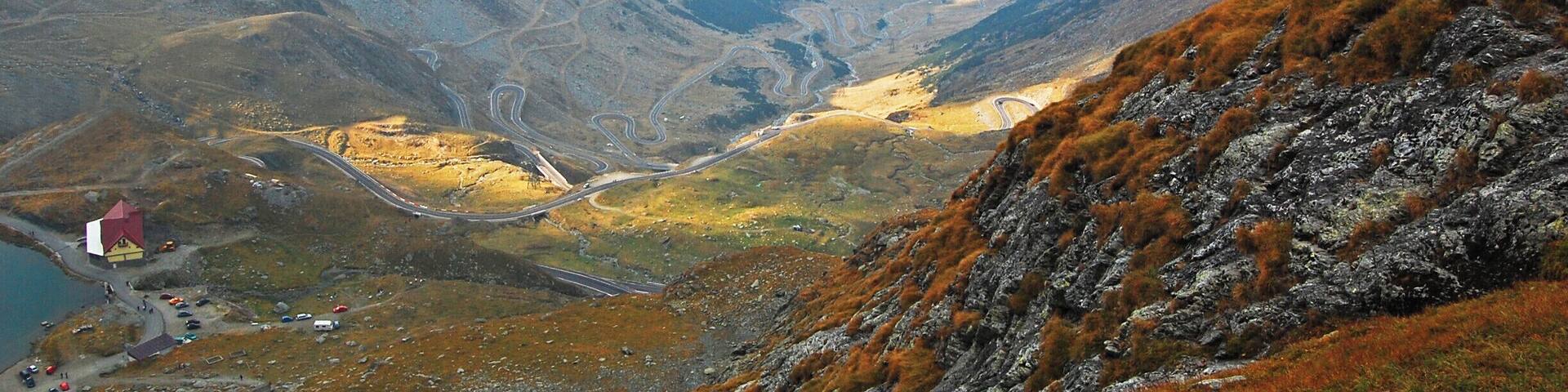 A mountainous landscape with winding roads and a small building near a body of water.