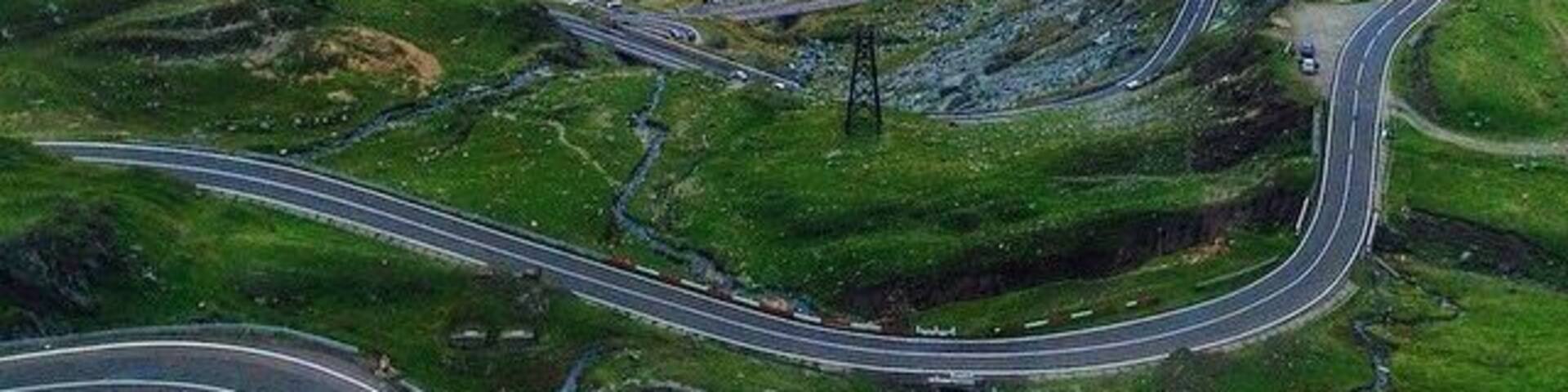 A winding mountain road through a valley with green hills and distant mountains.