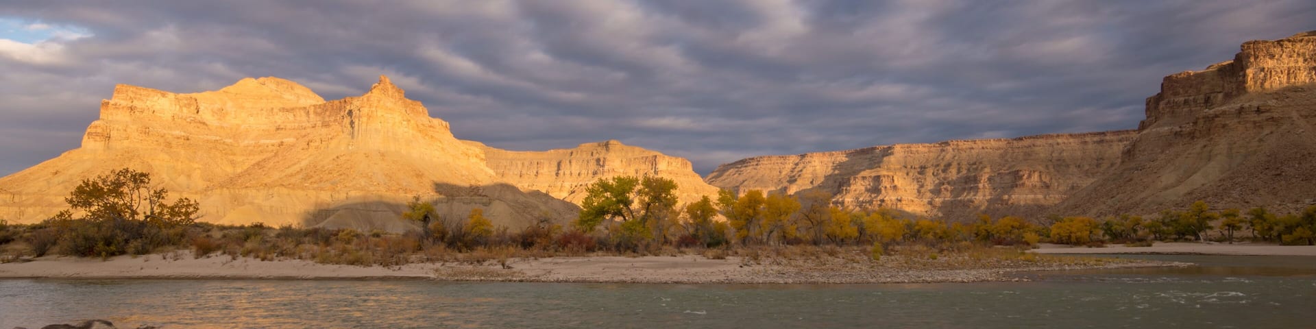 Sunlight shining through the clouds on desert landscape of Grays Canyon as the Green River flows past Swasey's Beach.