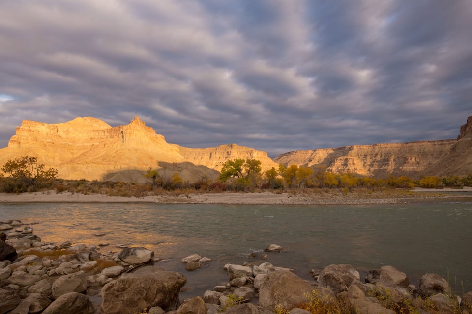 A river with rocky banks, a clear sky, and a mountain range in the background.