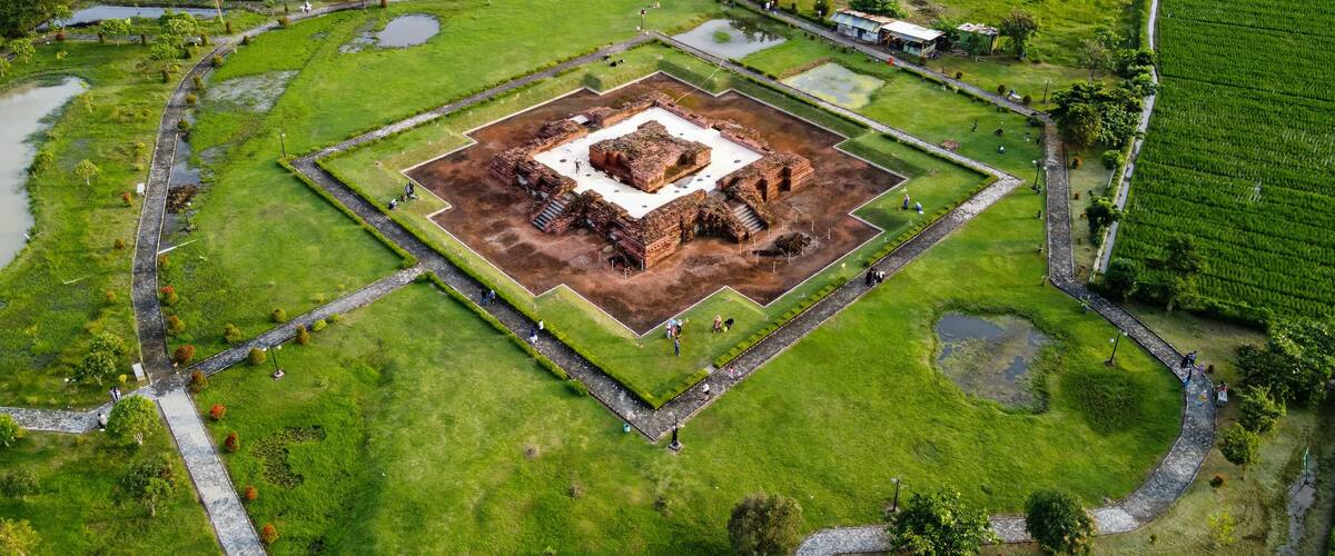 An aerial view of a historical site with a central square, surrounding pathways, and adjacent green fields.