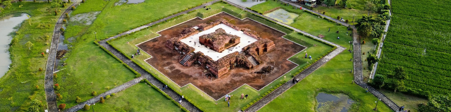 An aerial view of a historical site with a central square, surrounding pathways, and adjacent green fields.
