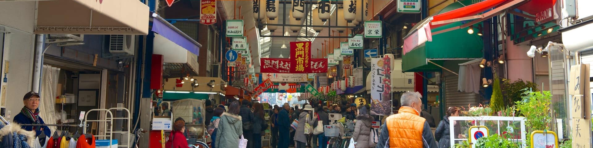 A busy market street with colorful banners and signs, including a 'No Entry' sign for vehicles.