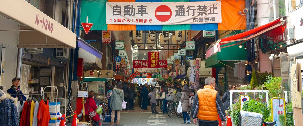 A busy market street with colorful banners and signs, including a 'No Entry' sign for vehicles.