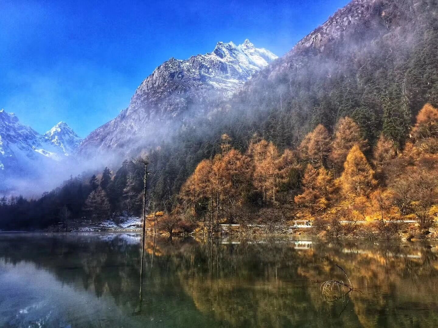 A mountain lake with reflections, autumn-colored trees, and snow-capped peaks.