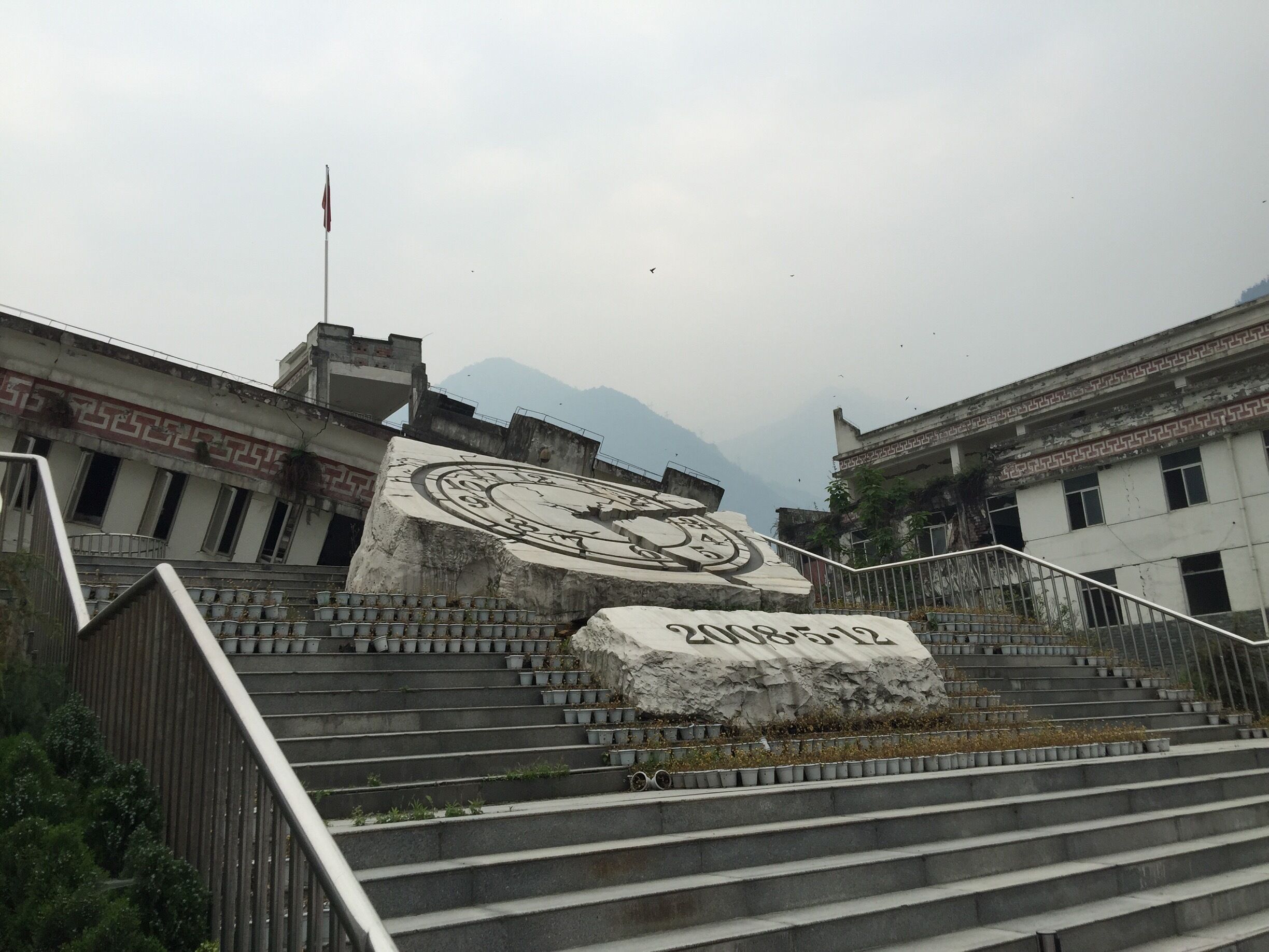 A staircase with a large rock inscribed with '2009-12' leading to a building with a flag.