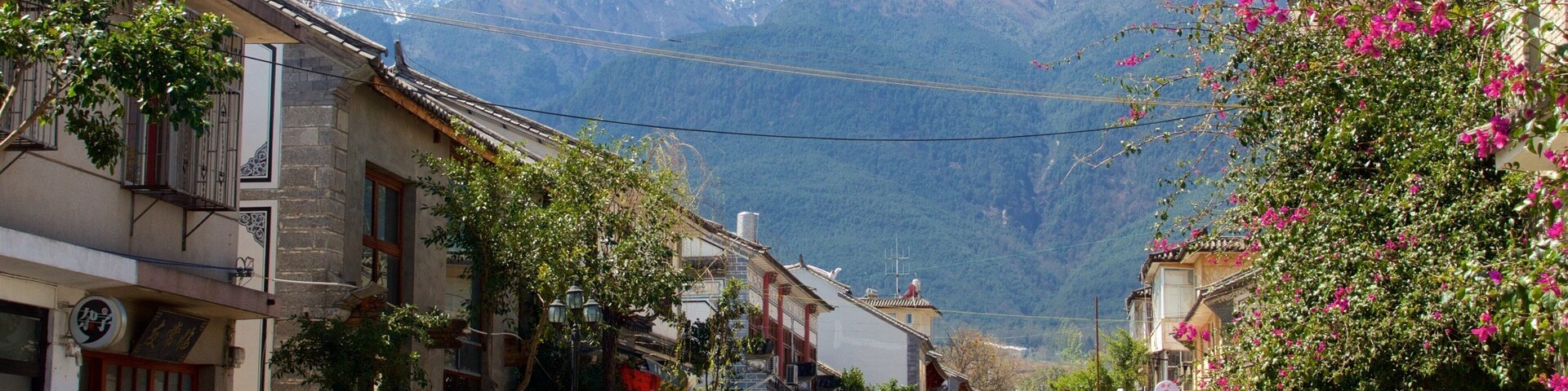 A street with traditional buildings, a tuk-tuk, and a mountain in the background.