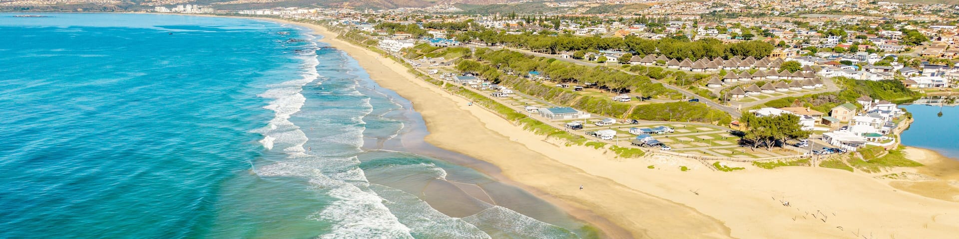 A coastal town with a sandy beach, clear blue waters, and residential buildings.