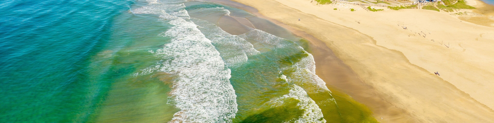 A coastal town with a sandy beach, clear blue waters, and residential buildings.
