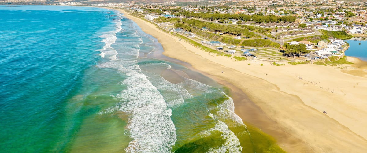 A coastal town with a sandy beach, clear blue waters, and residential buildings.