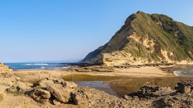 A coastal landscape with a rocky beach, a sandy shore, and a prominent cliff.