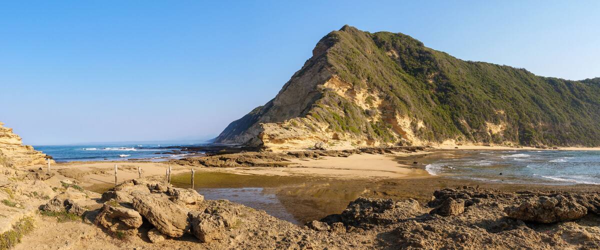 A coastal landscape with a rocky beach, a sandy shore, and a prominent cliff.