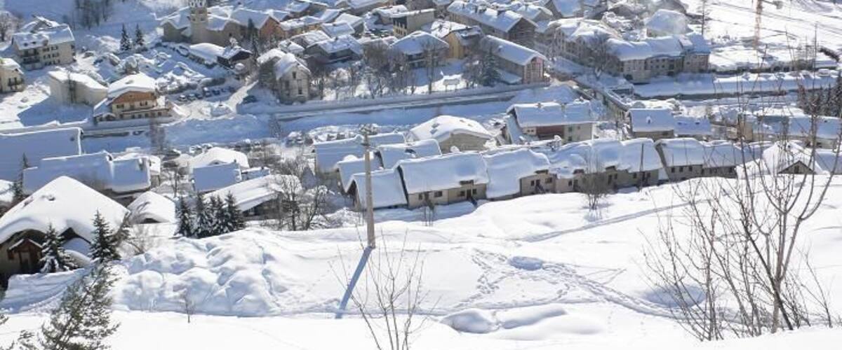 A snow-covered village nestled in a valley with houses and buildings, surrounded by mountains.