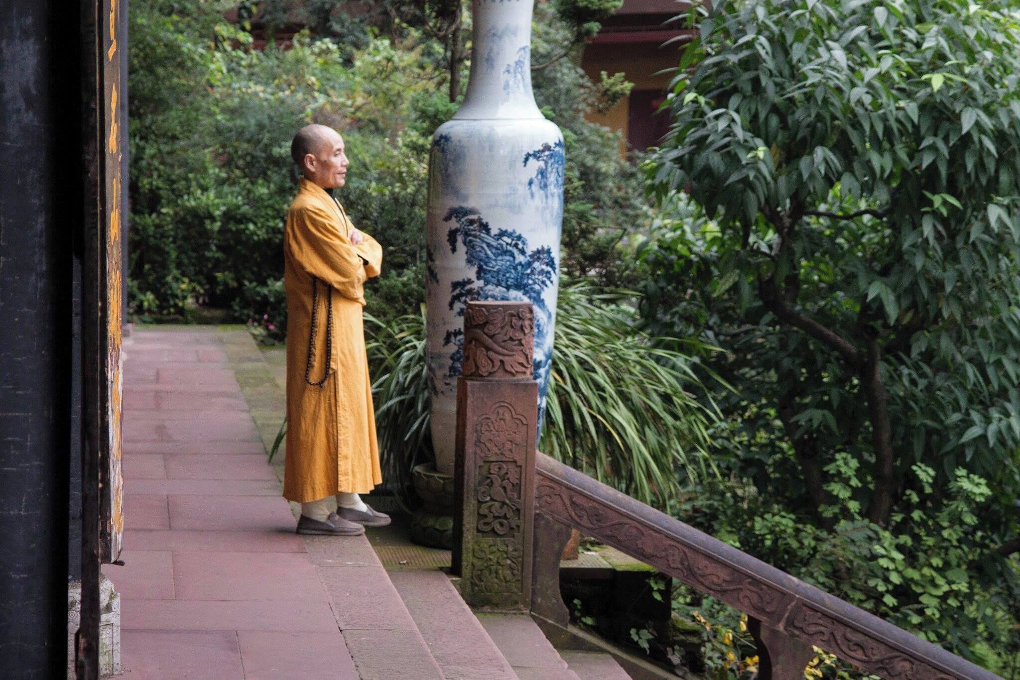 A monk in traditional yellow robes standing on a pathway next to a large blue and white vase.