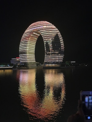 A brightly lit, circular architectural structure reflecting on water at night.
