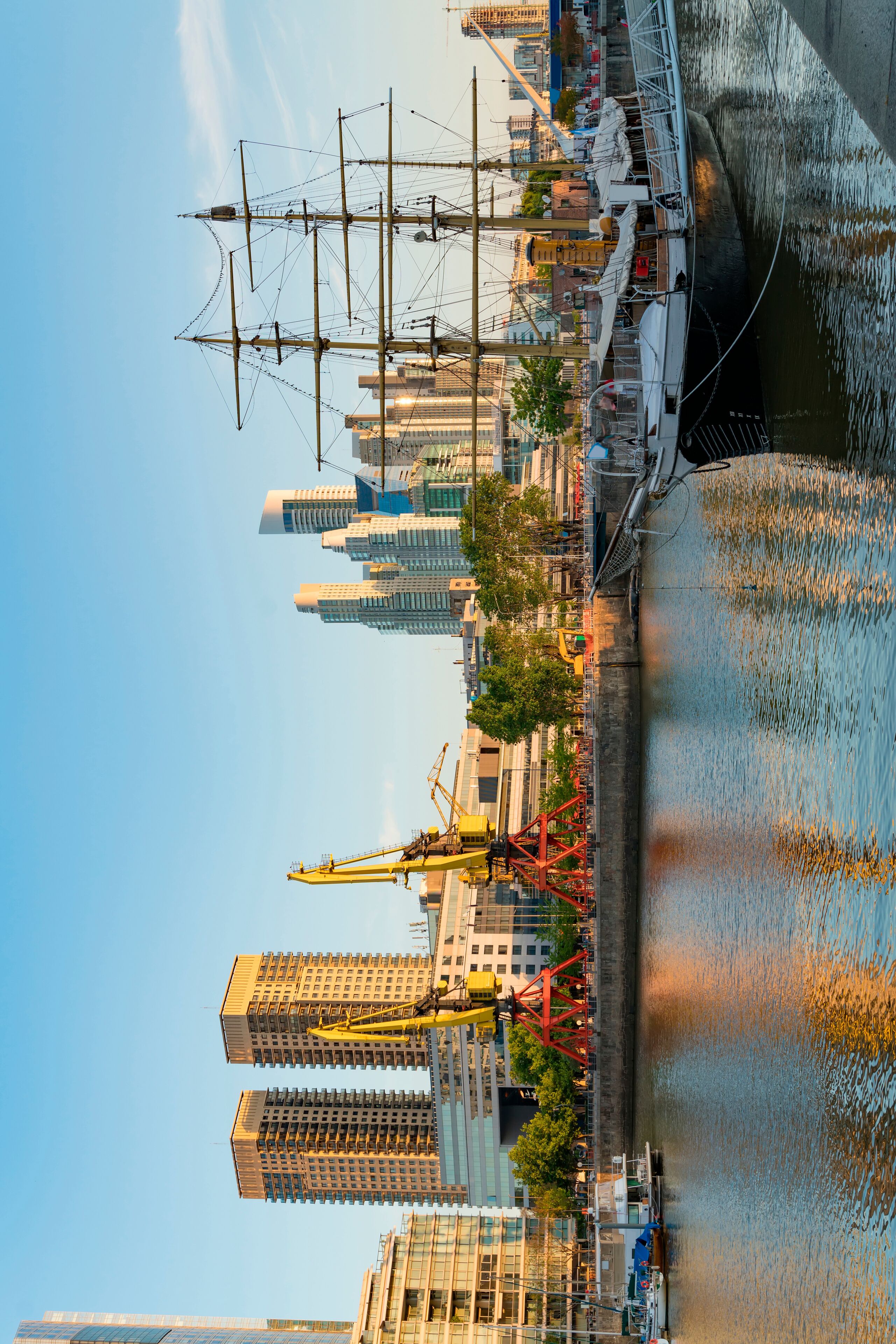 Un río con un barco mercante alto atracado a la derecha, rodeado de edificios modernos y grúas de construcción.