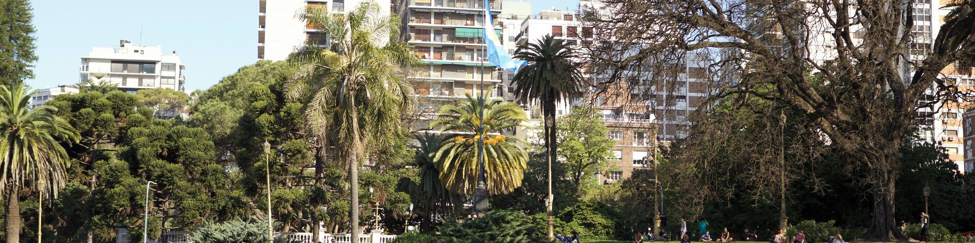A park with people relaxing on the grass, surrounded by tall buildings and trees.