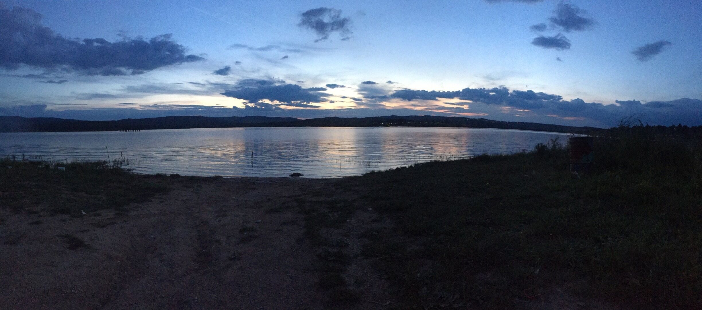 A calm lake at dusk with a clear sky and distant mountains.