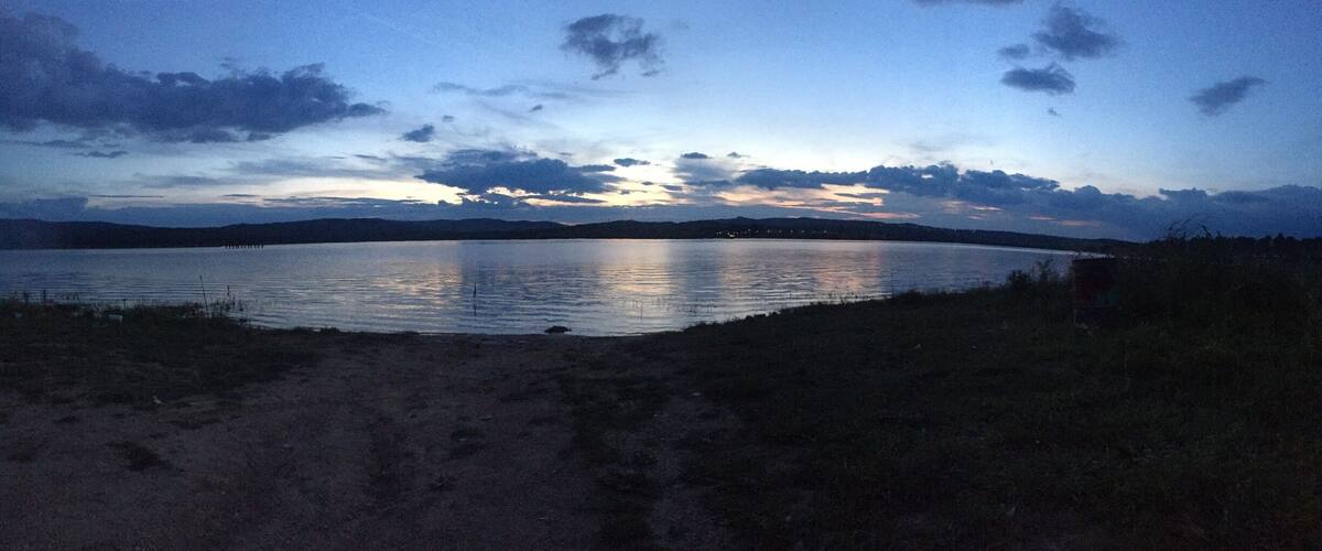 A calm lake at dusk with a clear sky and distant mountains.