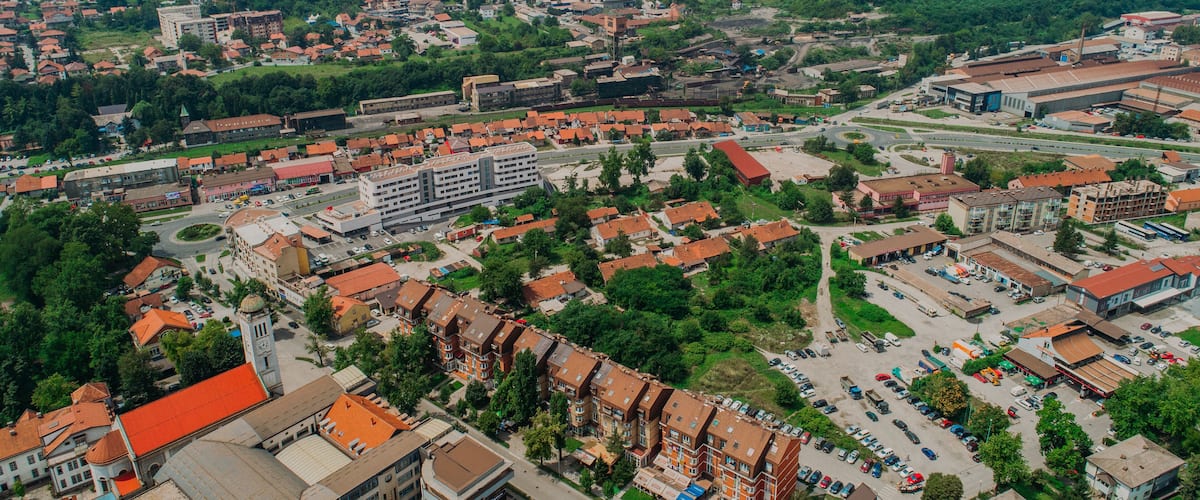 An aerial view of a town with a mix of residential and commercial buildings, surrounded by green hills.