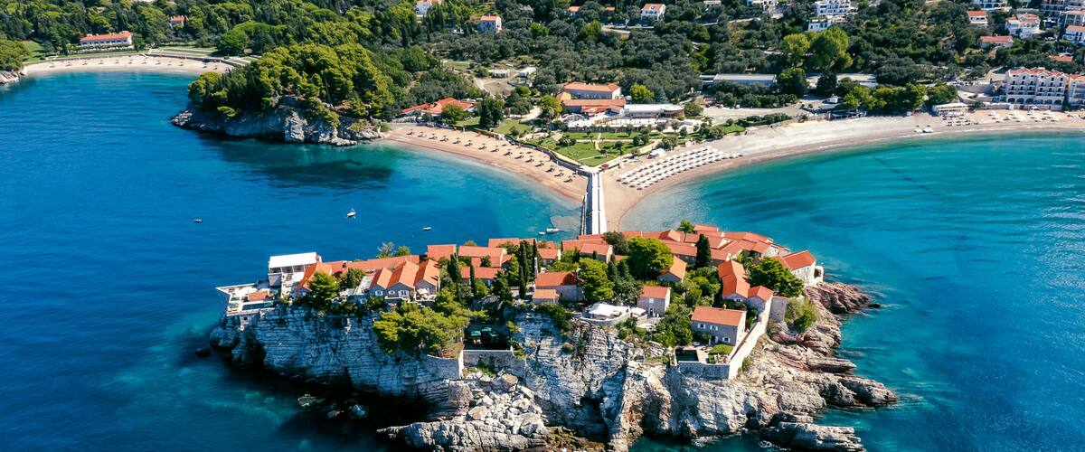 A coastal town with a prominent rocky peninsula, clear blue waters, and a beach.