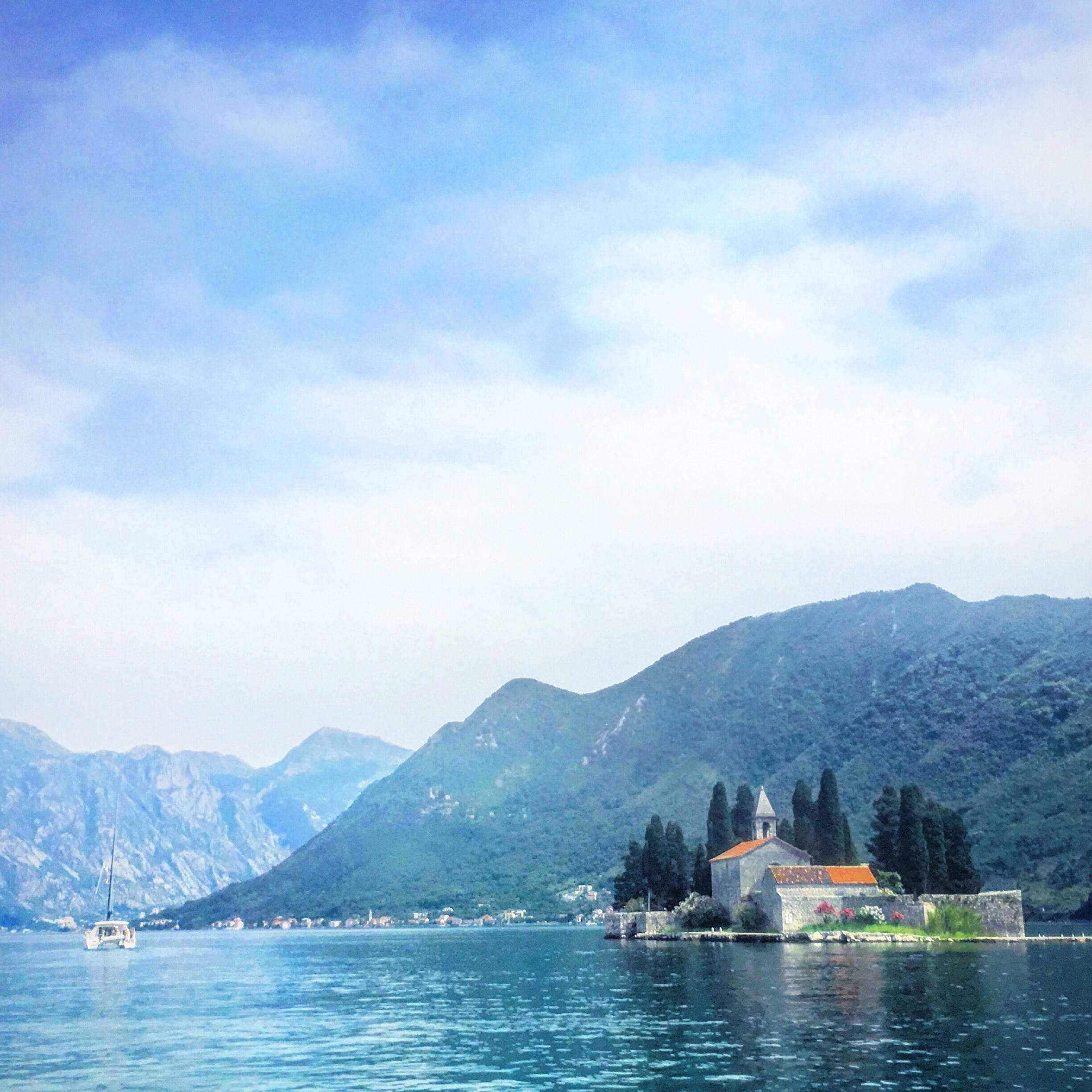 A coastal town with a church on a small island, surrounded by mountains and a clear sky.