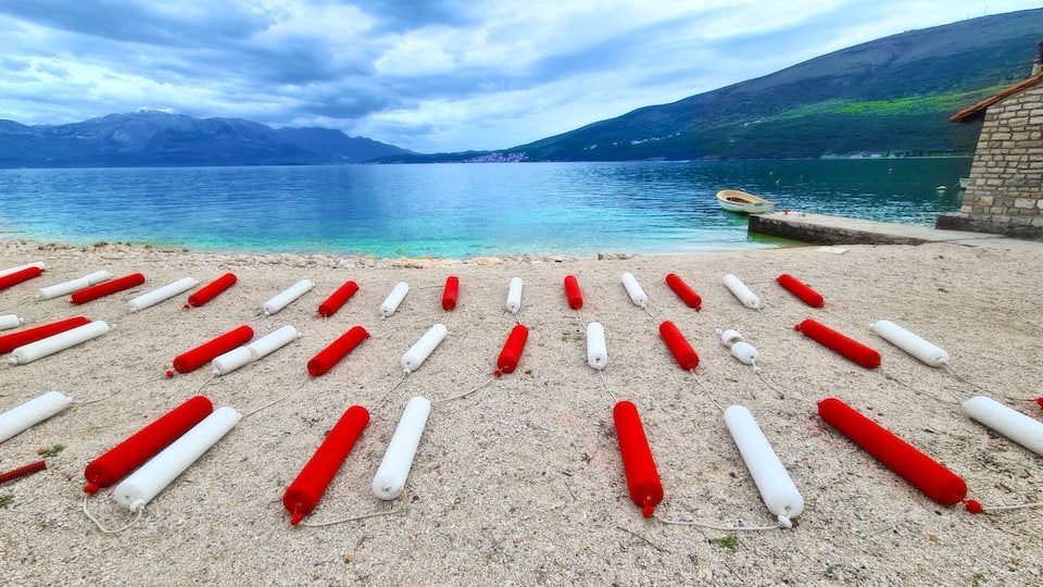 A lake with mountains in the background and buoys arranged on the shore.