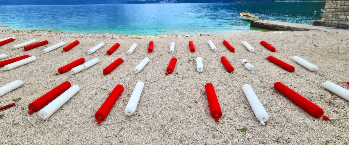 A lake with mountains in the background and buoys arranged on the shore.
