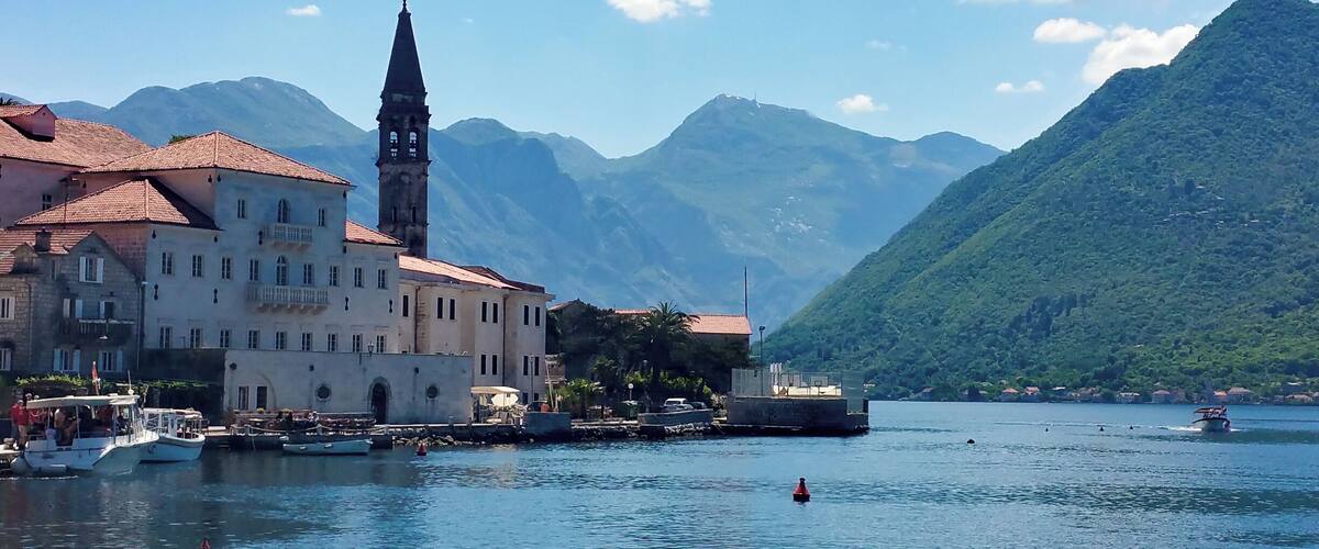 Uma vila costeira com uma igreja imponente, barcos e montanhas ao fundo.