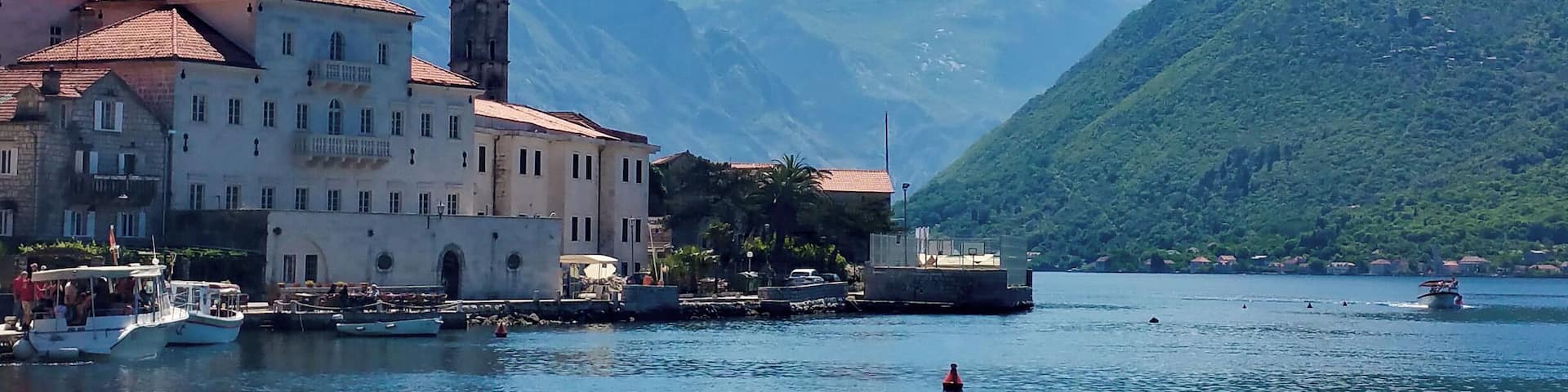 A coastal town with a prominent church, boats, and mountains in the background.