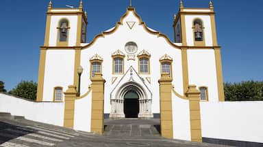 A church with a white facade and yellow trim, featuring a central entrance with a pointed arch and a bell tower on each side.