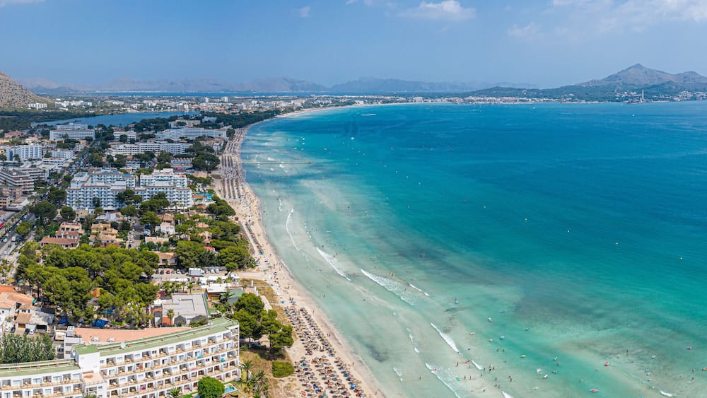 A coastal city with a beach, buildings, and mountains in the background.