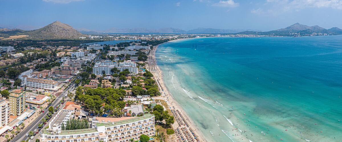 A coastal city with a beach, buildings, and mountains in the background.