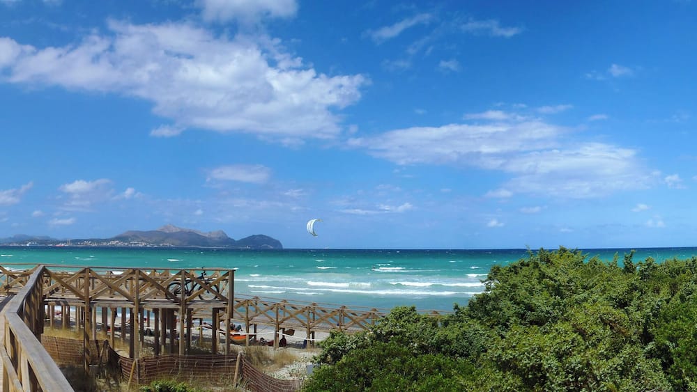 Une promenade en bois qui mène à une plage aux eaux turquoise et sous un ciel dégagé.