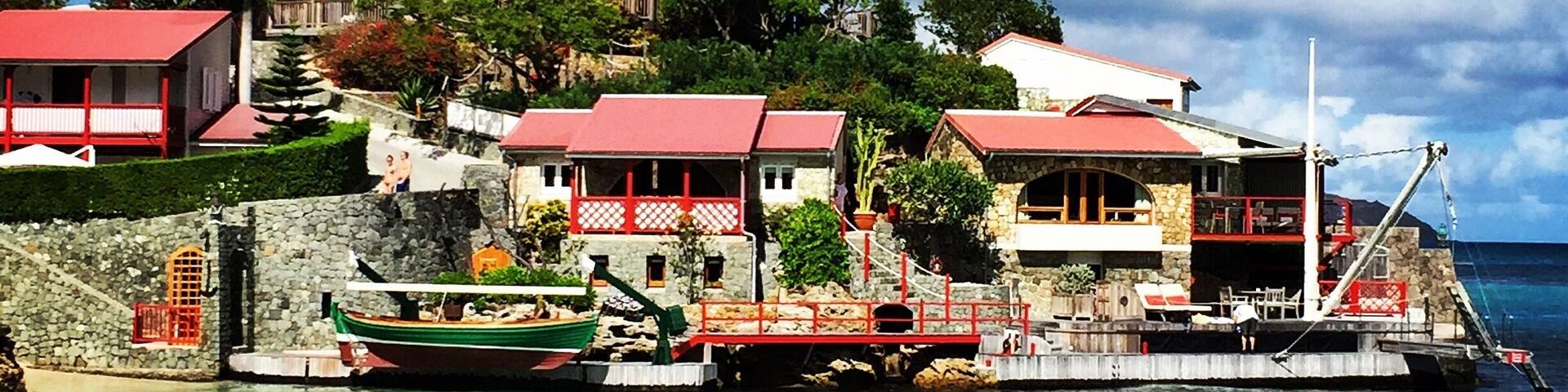A coastal village with red-roofed buildings, clear turquoise waters, and a stone staircase leading up to the houses.